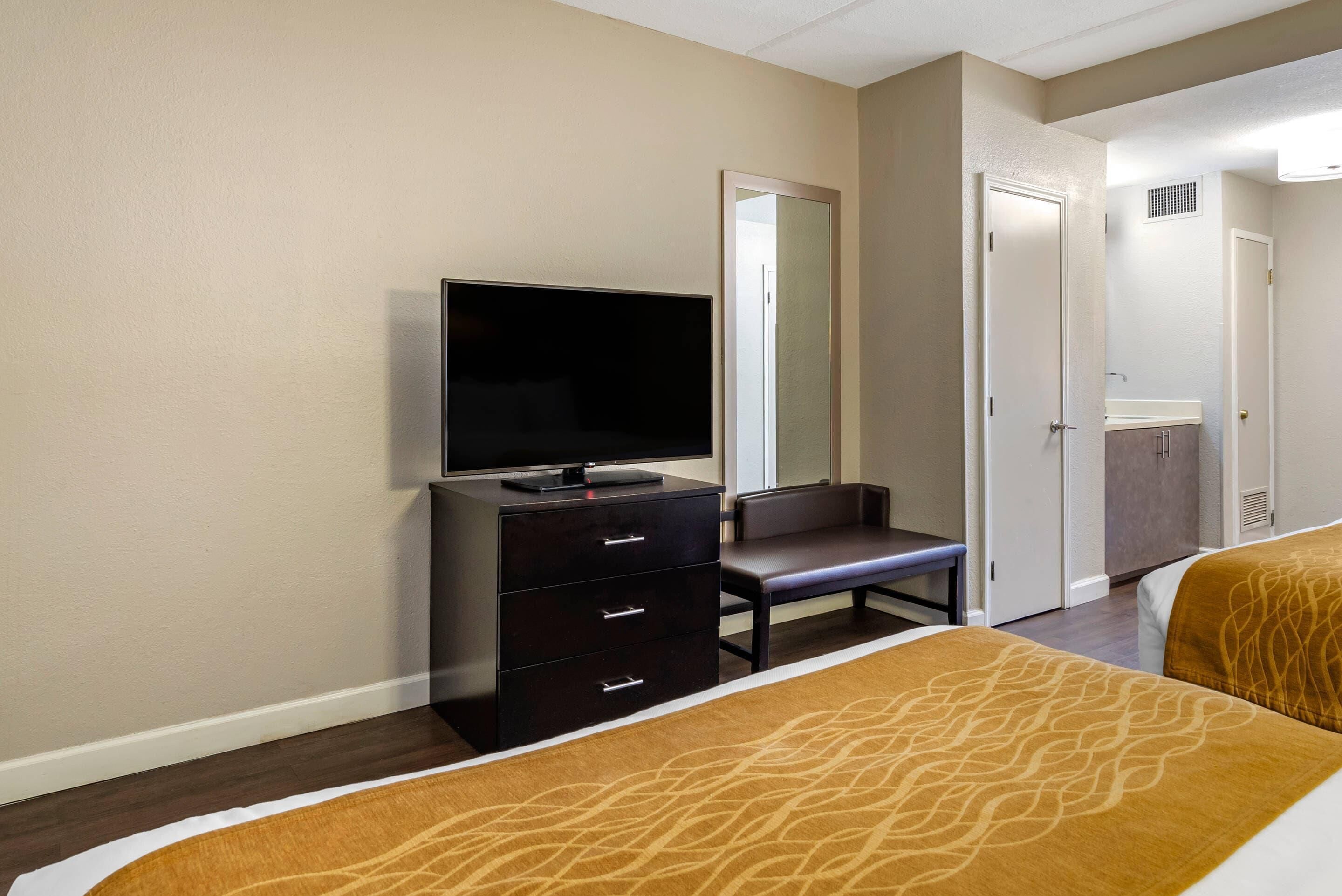 Une chambre d’hôtel avec un lit, un téléviseur posé sur une commode, une chaise et une salle de bain visible à travers une porte ouverte.