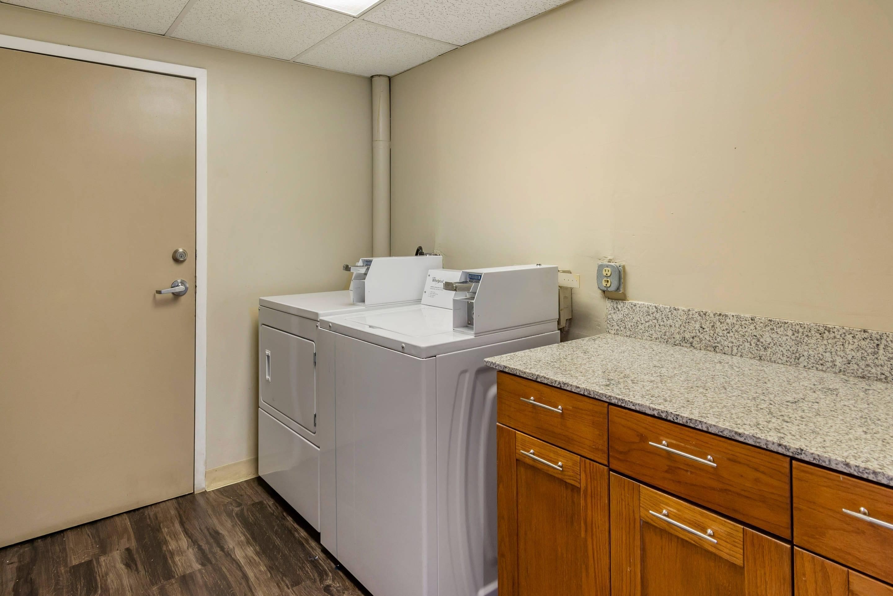 A laundry room with a washing machine, dryer, and wooden cabinets.
