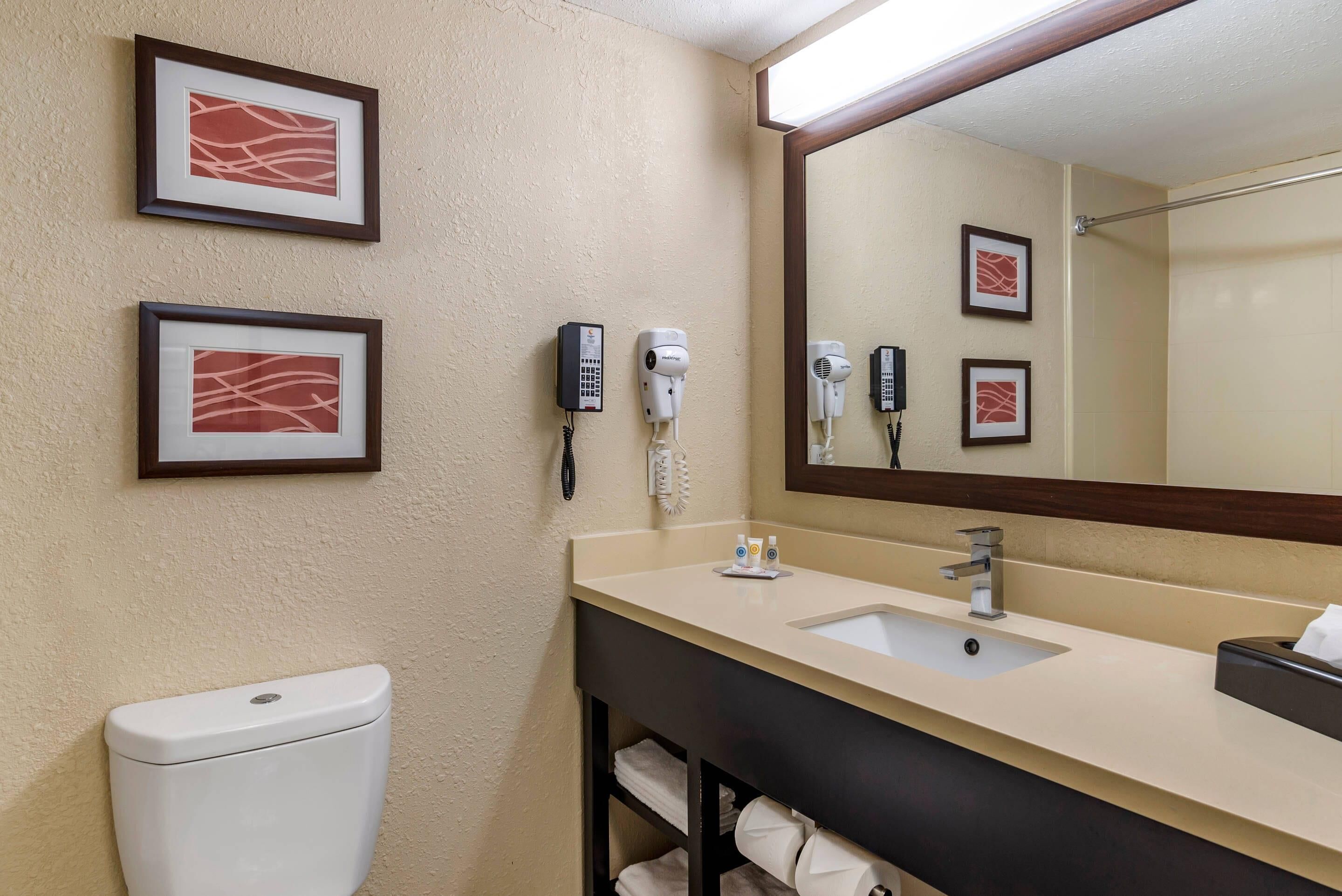 A bathroom with a toilet, sink, and two hair dryers mounted on the wall.