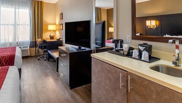 A hotel room with a bed, desk, TV, and a bathroom with a sink and mirror. - Comfort Inn & Suites near Six Flags (Lithia Springs)