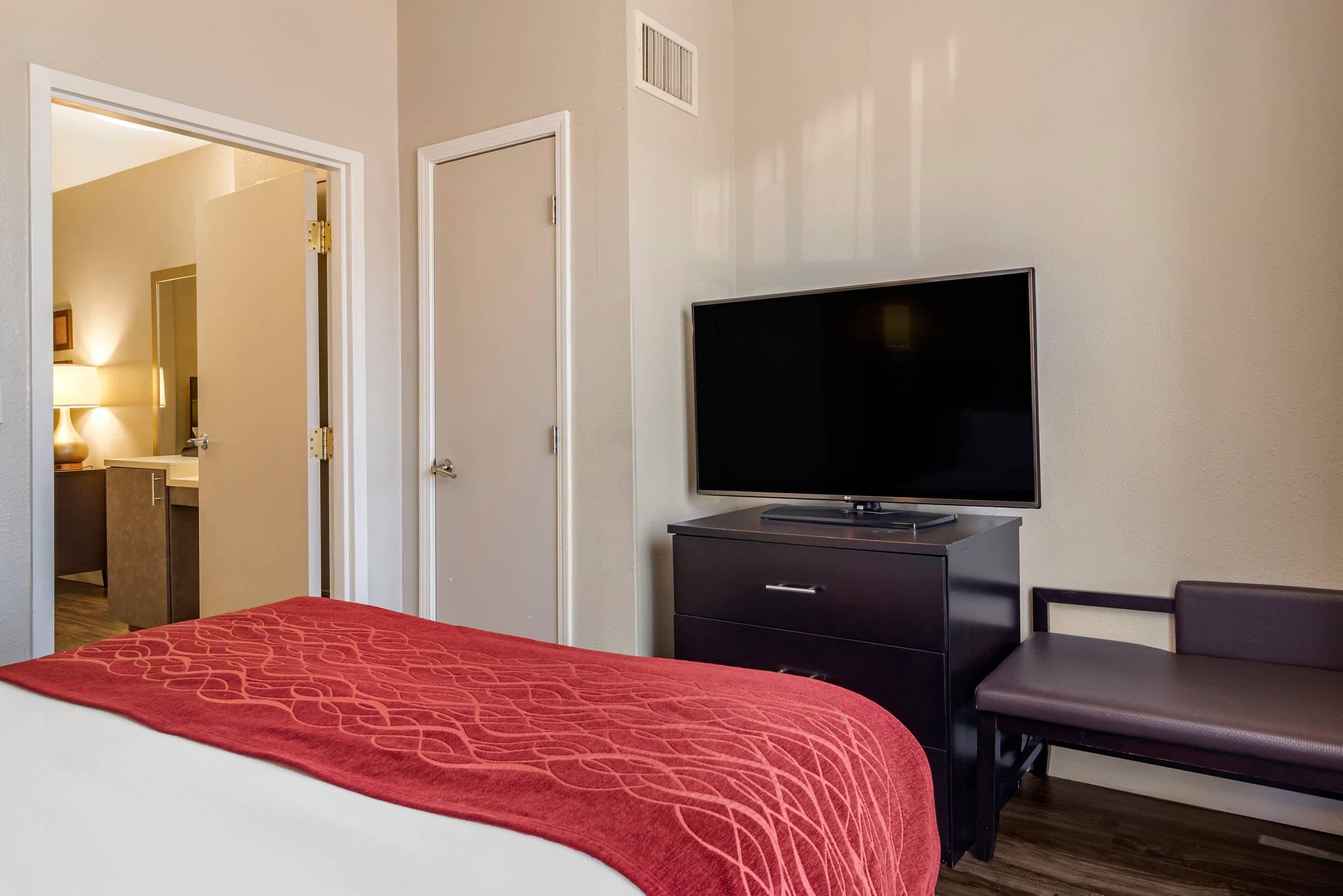 A hotel room with a bed, a television on a dresser, a desk, and a chair.