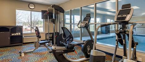 Un gimnasio con equipamiento cardiovascular, una máquina de remo y una banca para pesas.