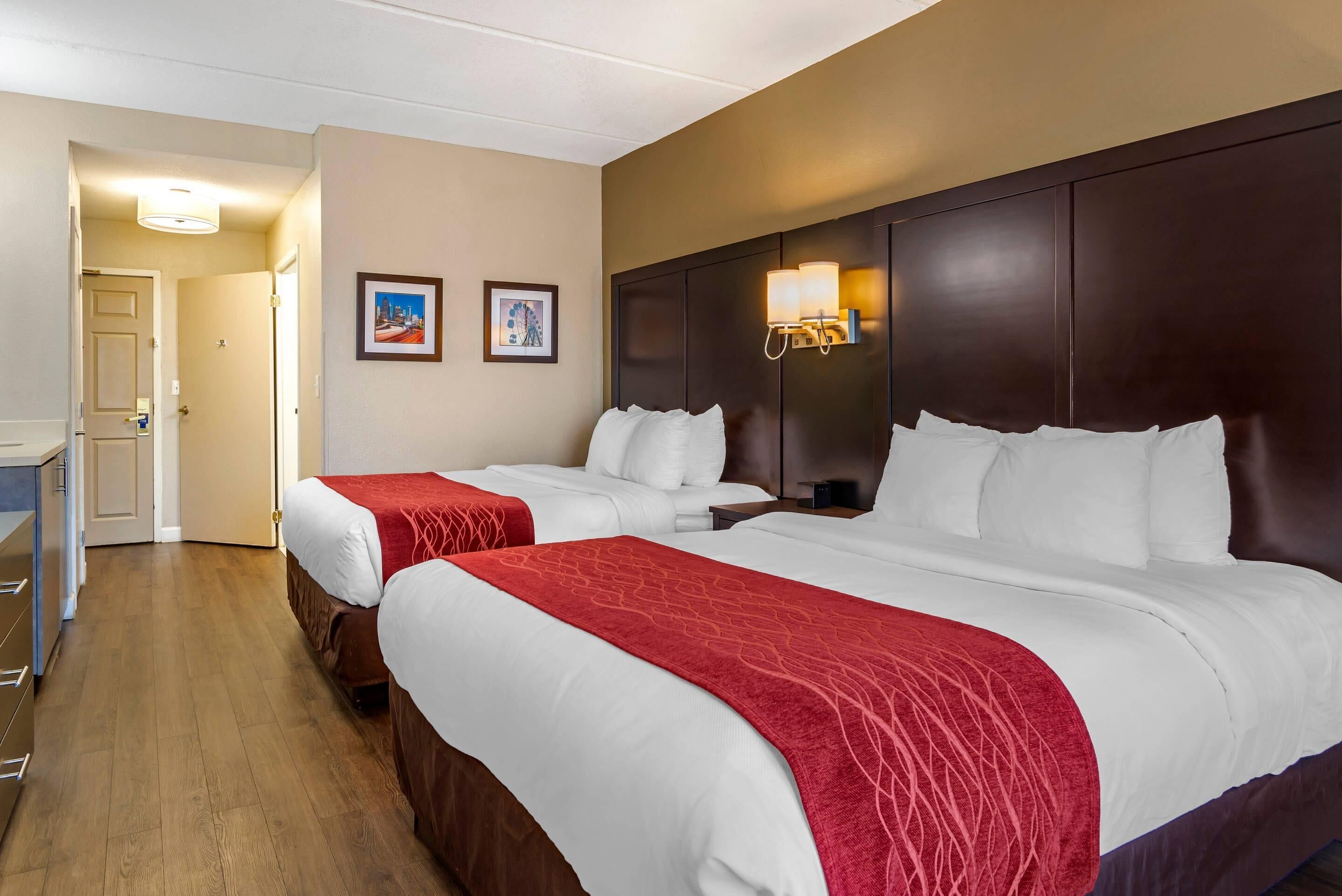 Ein Hotelzimmer mit zwei Betten, Holzboden, dunklem Kopfteil und einer Wandleuchte.
