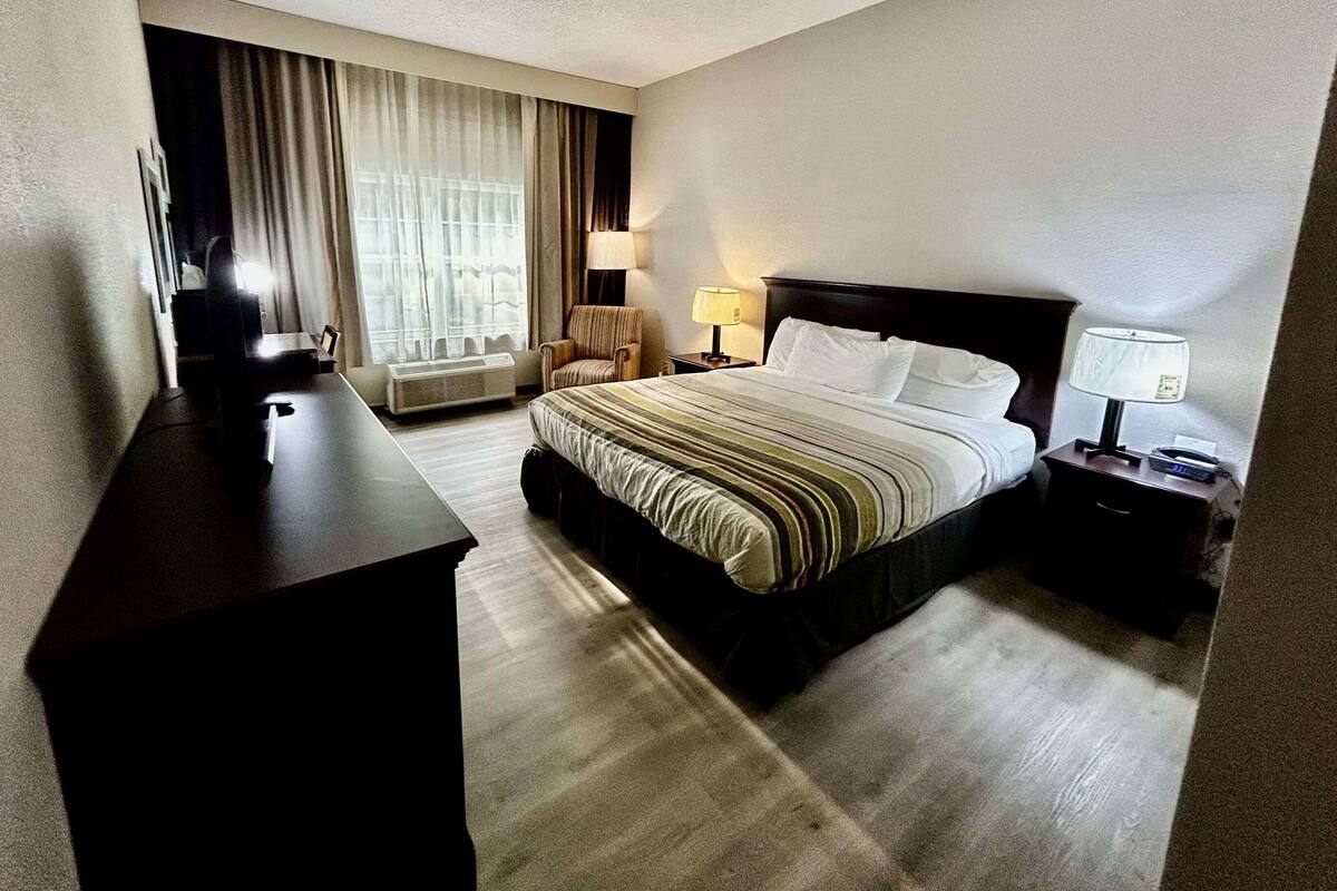 A hotel room with a bed, a desk, a chair, a lamp, and a window with curtains.