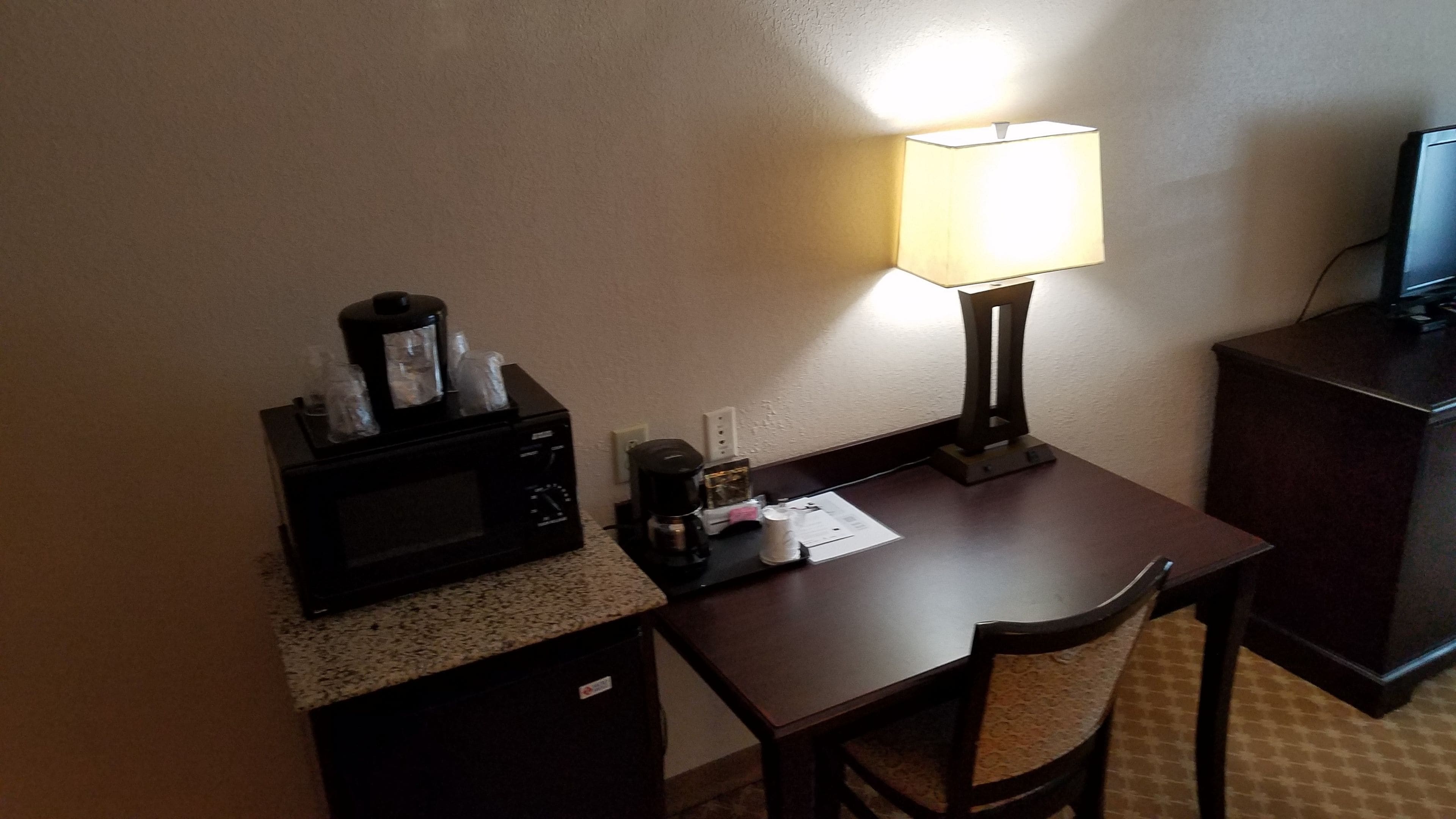 A small hotel room with a kitchenette, a microwave, a coffee maker, a lamp, and a desk.