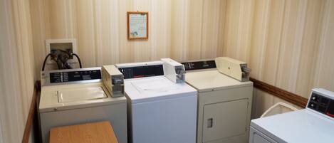 A laundry room with three washing machines and a dryer, a wooden table, and a wall-mounted sign.