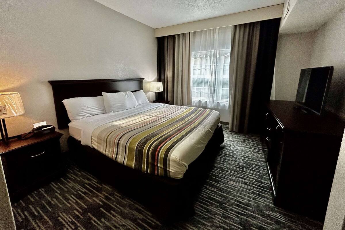A hotel room with a large bed, a nightstand with a lamp, a dresser, and a television.
