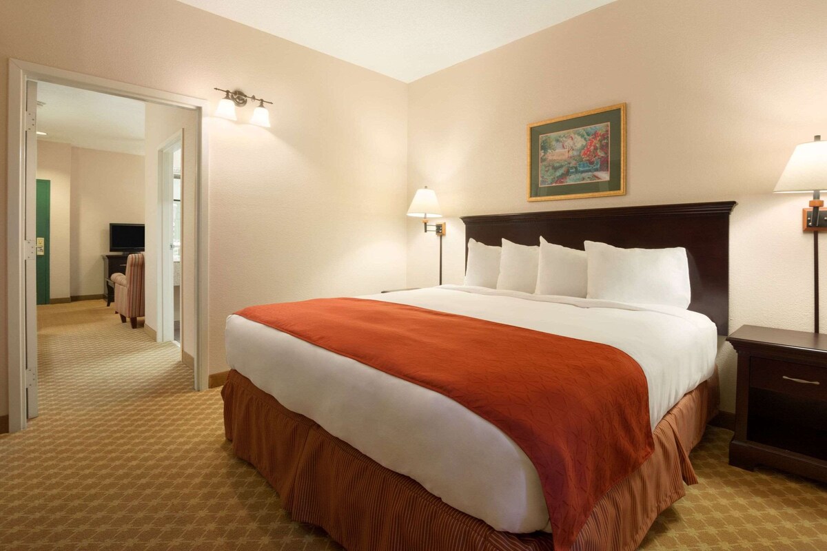 A hotel room with a large bed, two bedside lamps, a painting on the wall, and a mirror in the corner.