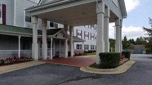 A building with a covered entrance, multiple windows, and a brick pathway leading to the entrance.