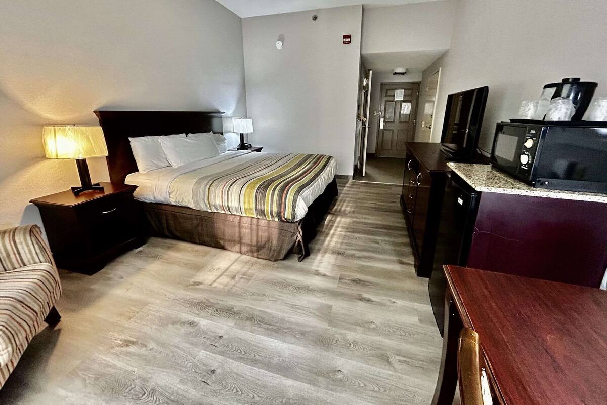 A hotel room with a bed, a desk, a chair, a microwave, and a television.