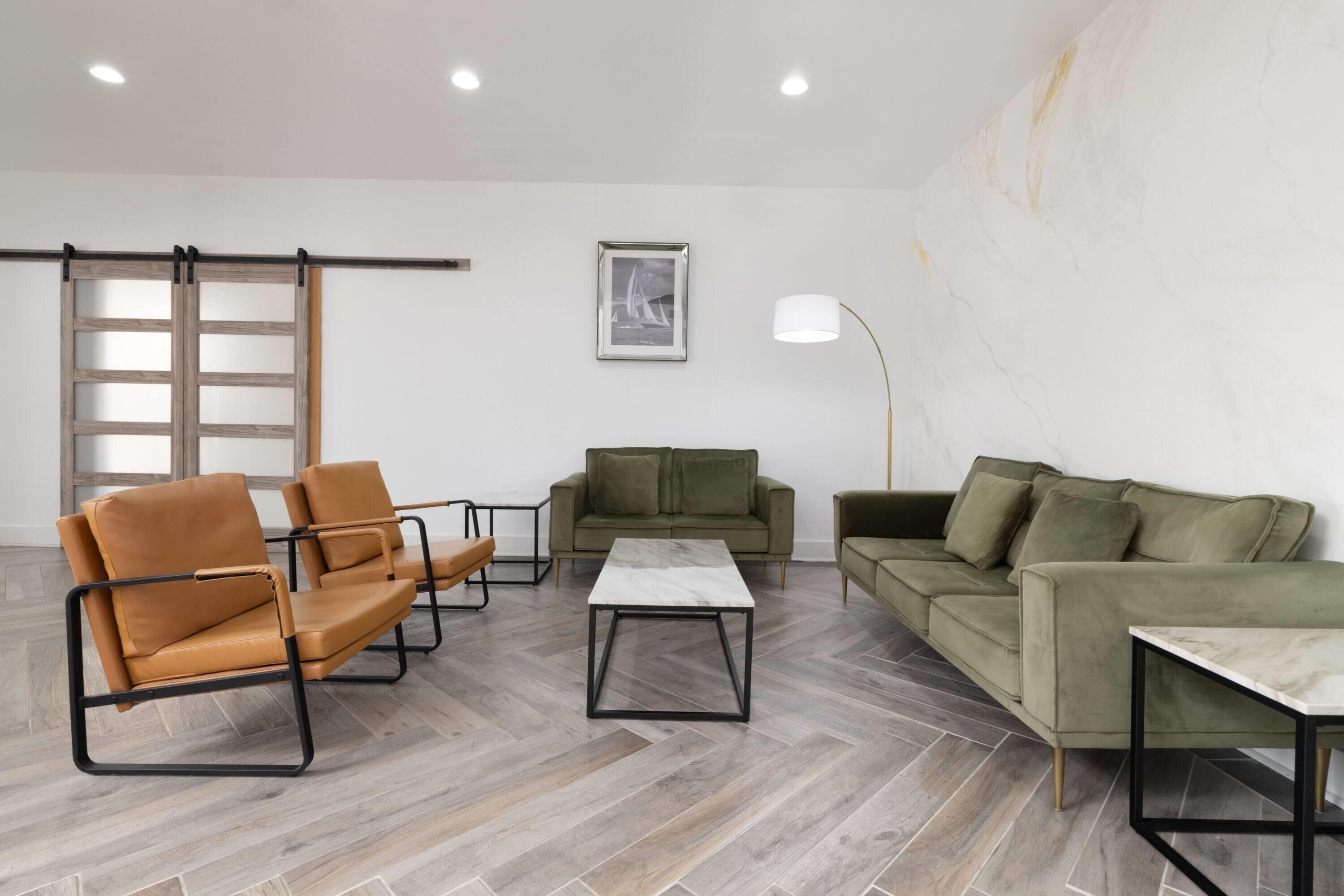 Un saló modern amb un paviment de fusta en disseny de petxina, una taula de centre de marbre blanc i dos sofàs verds.