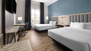 Une chambre d’hôtel avec deux lits, un bureau, une chaise, une télévision et une fenêtre avec des rideaux.
