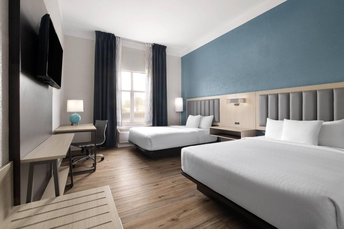 Une chambre d’hôtel avec deux lits, un bureau, une chaise, une télévision et une fenêtre avec des rideaux.