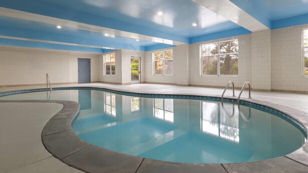 Une piscine intérieure à l’eau d’un bleu cristallin, entourée de murs recouverts de carreaux blancs et surmontée d’un plafond bleu.