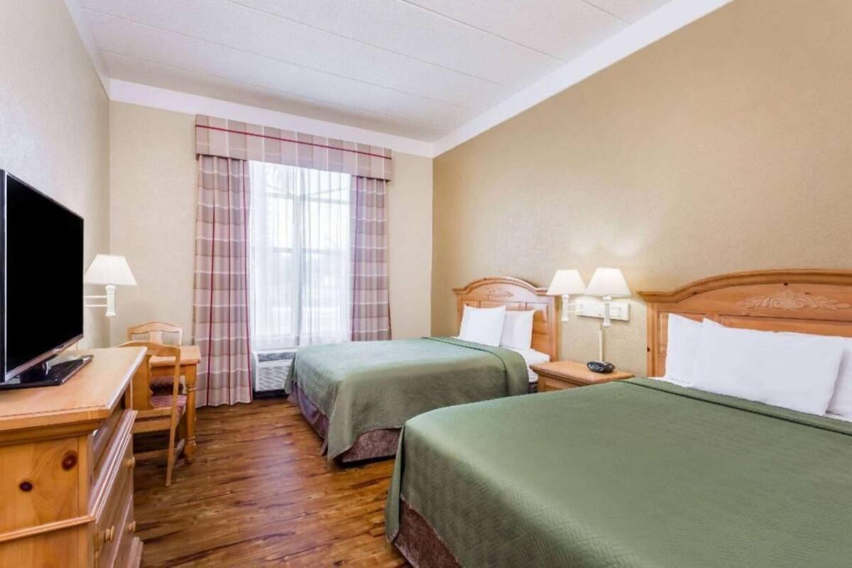 Une chambre d’hôtel avec deux lits, une télévision, un bureau avec une lampe et une fenêtre avec des rideaux.