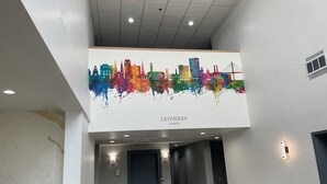 Un hall d’hôtel agrémenté d’une fresque murale représentant un paysage urbain aux couleurs vives, d’un design moderne au niveau du plafond et d’un espace propre et bien éclairé.