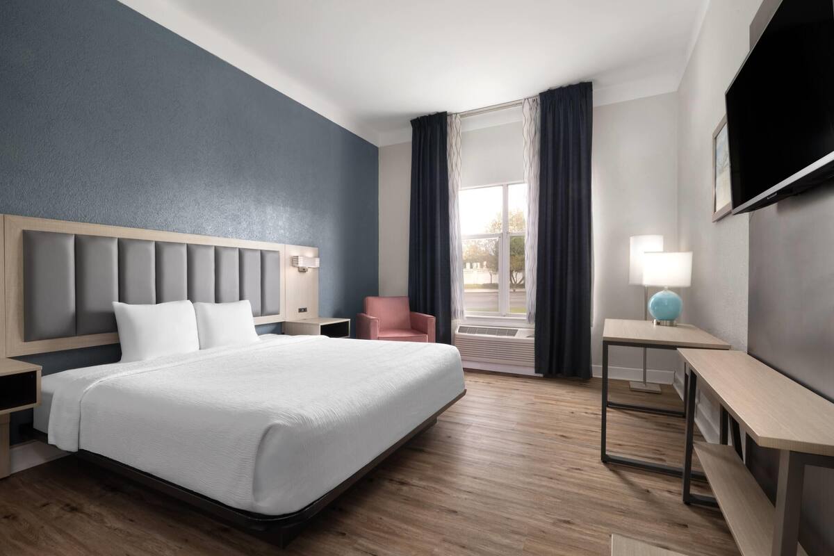 Une chambre d’hôtel avec un grand lit, un bureau, une chaise, une télévision et une fenêtre avec des rideaux.
