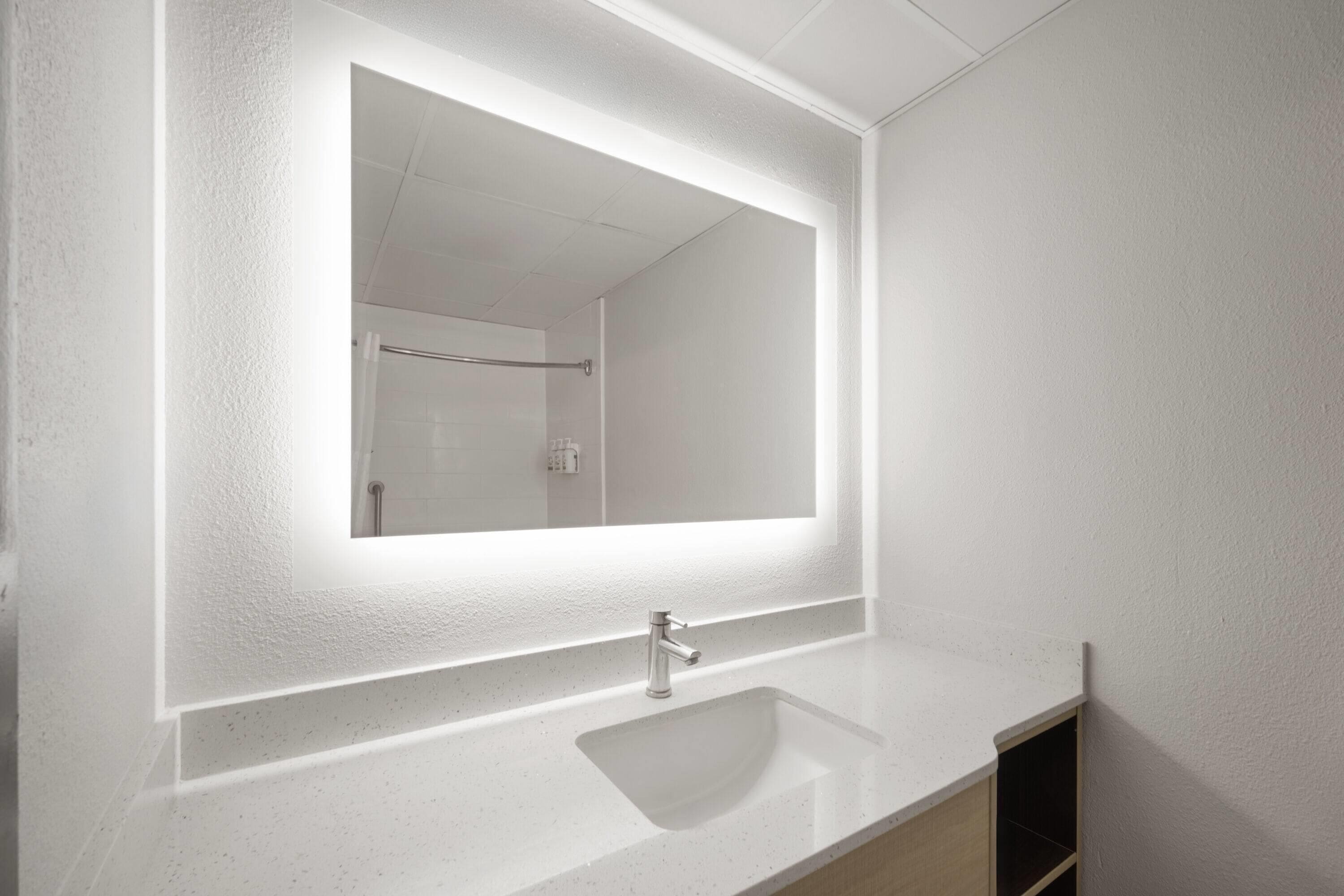 A bathroom with a white sink, a mirror, and a shower visible in the background.