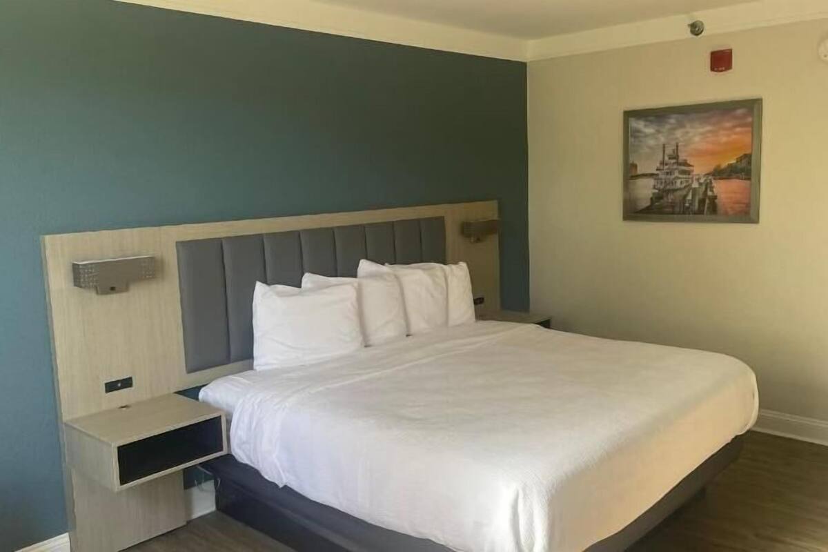 Une chambre d’hôtel avec un lit, une table de chevet, une lampe fixée au mur et un tableau.