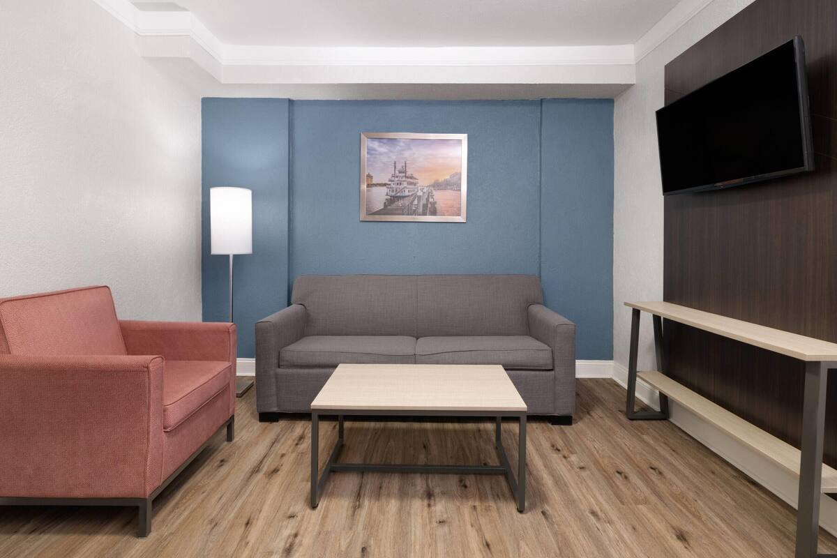Un salon moderne avec un canapé gris, un fauteuil rouge, une table basse en bois, un tableau encadré accroché au mur et un téléviseur fixé au mur.