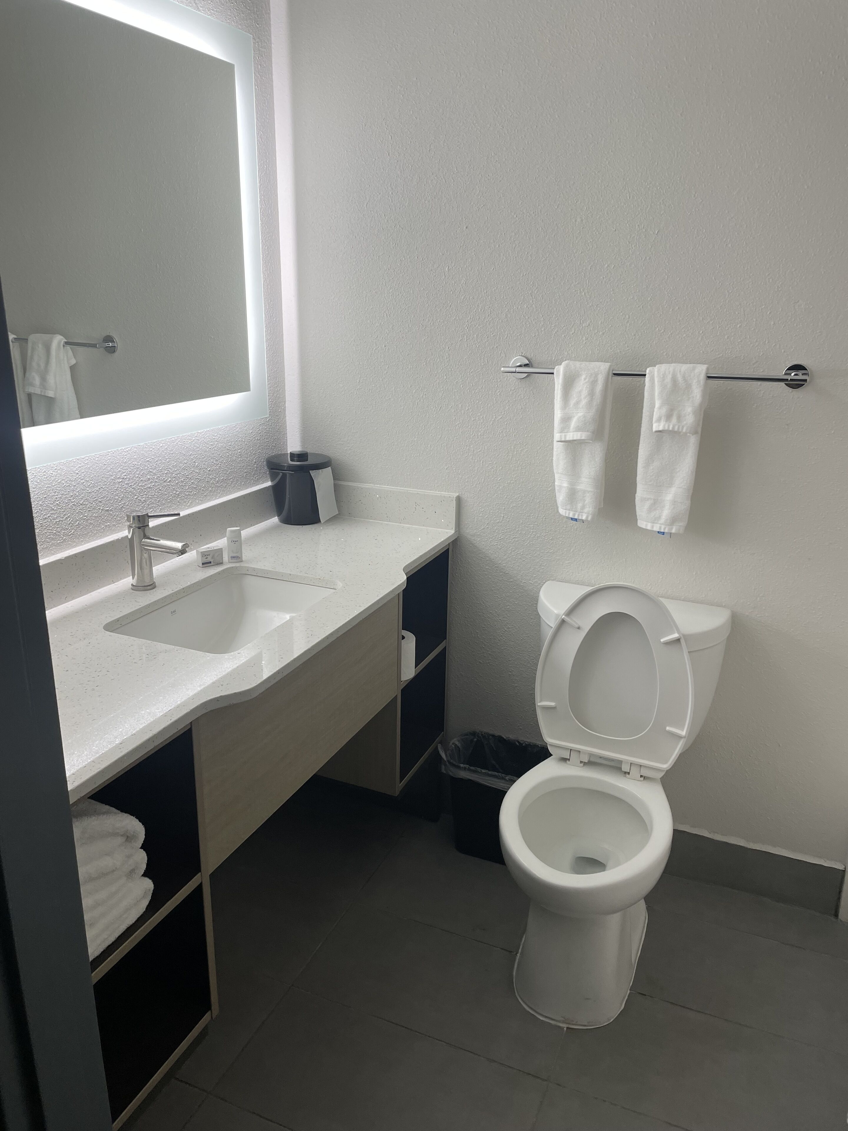 A modern bathroom with a white sink, mirror, and toilet. There are two towels hanging on a towel rack.