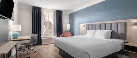 Ett modernt hotellrum med en stor säng, ett skrivbord, en stol, en TV och ett fönster med gardiner.