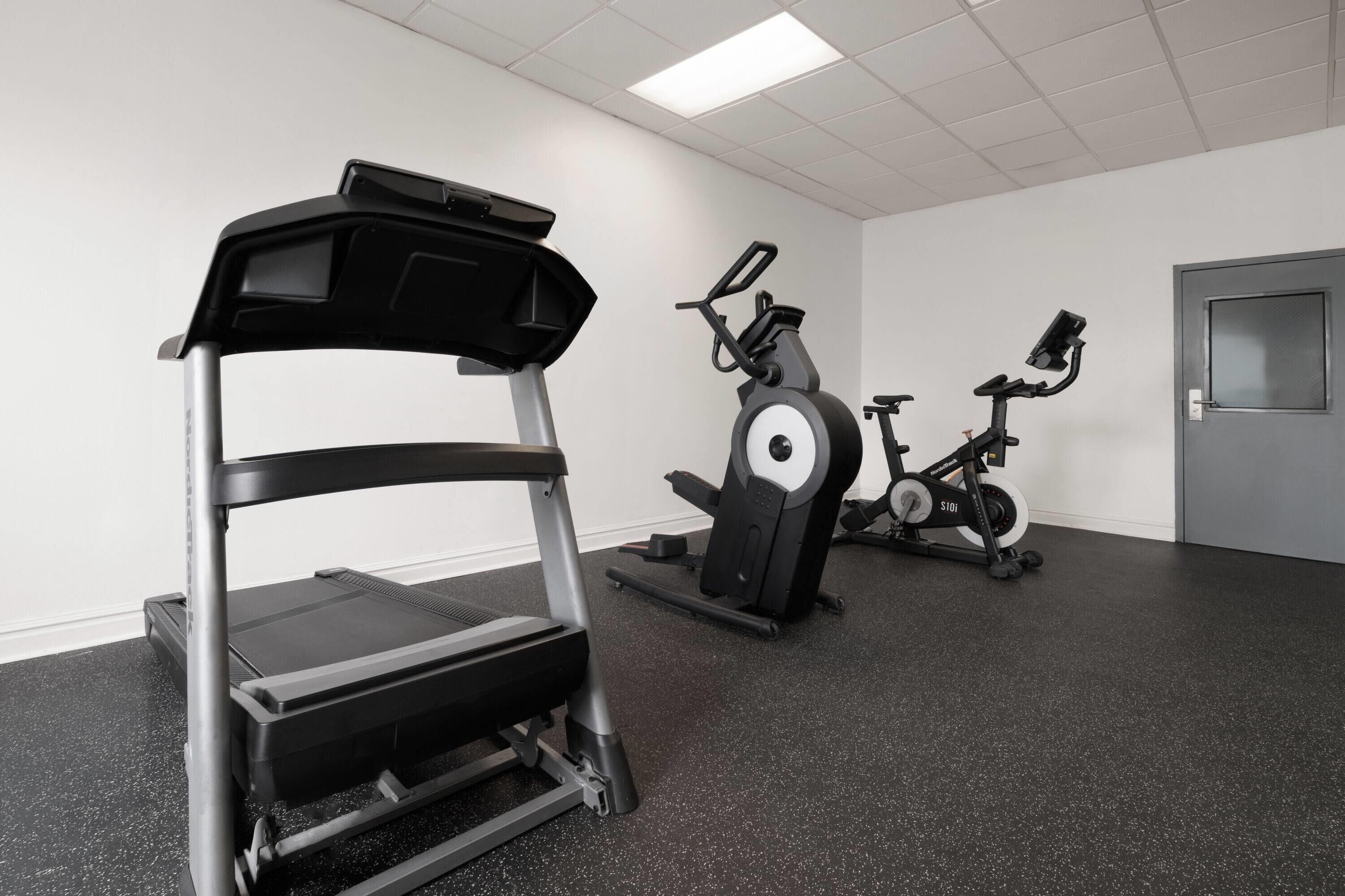 Un gimnasio con cinta de correr, bicicleta estática y máquina elíptica.