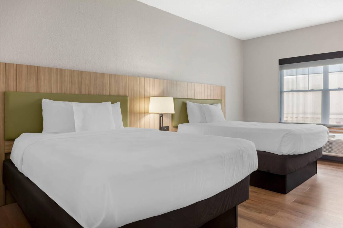 A hotel room with two beds, a wooden headboard, a window, and a lamp.