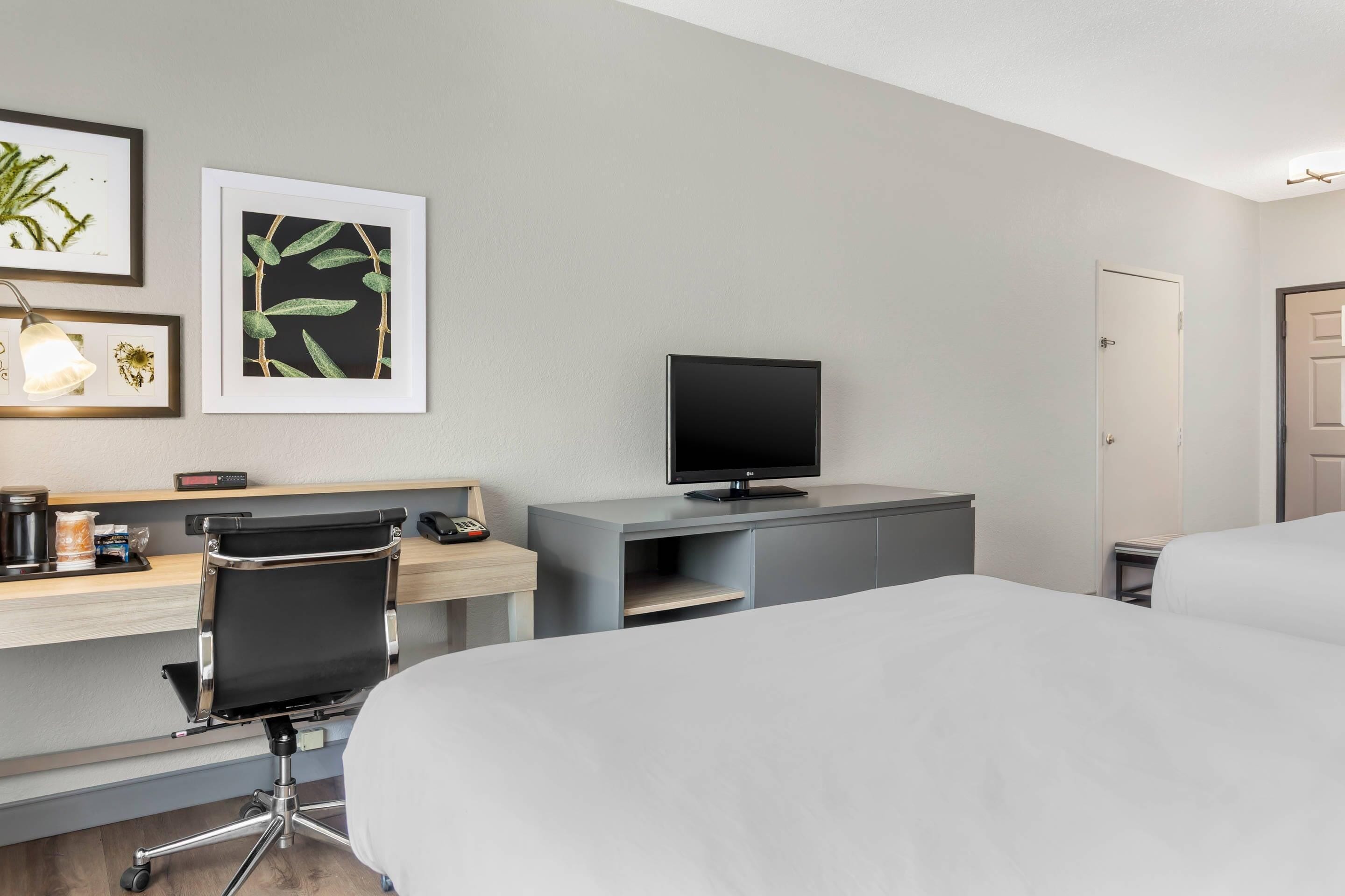 Hotellihuone, jossa on sänky, työpöytä, tuoli, televisio ja taideteos seinällä.