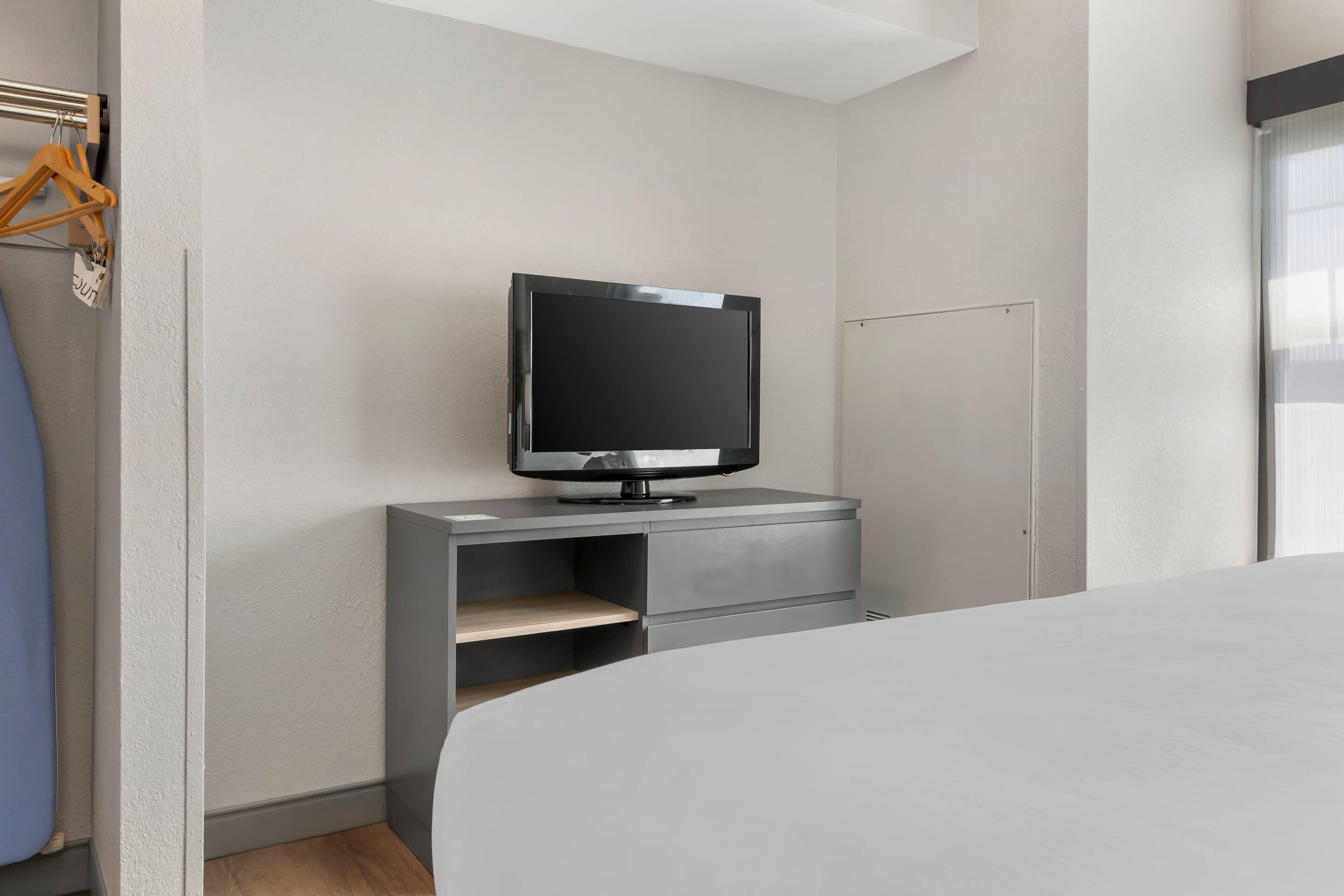 A modern hotel room with a bed, a TV on a grey console, and a wardrobe.