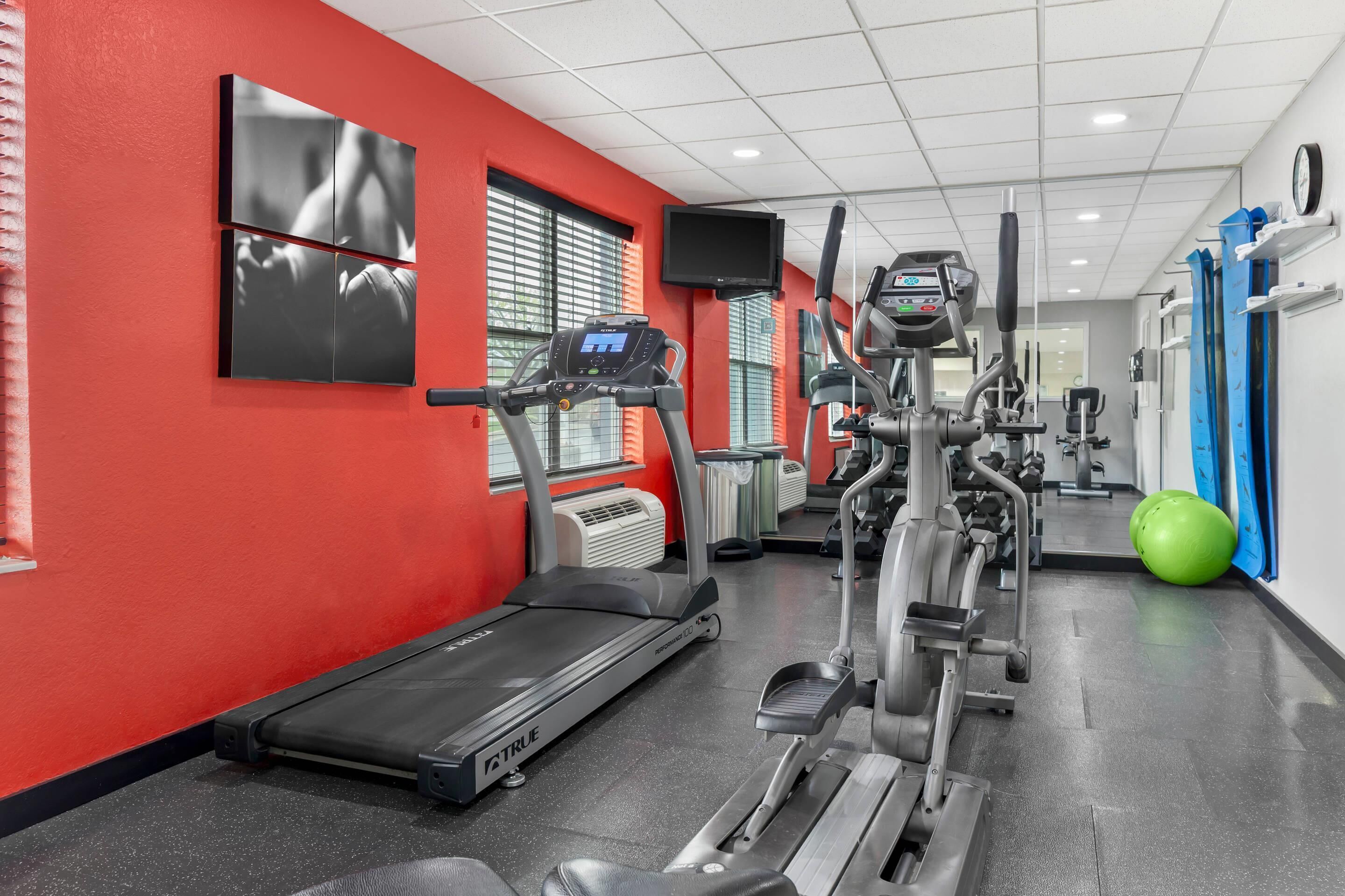 Un gimnasio con cintas de correr, elípticas y una pelota de ejercicio verde.