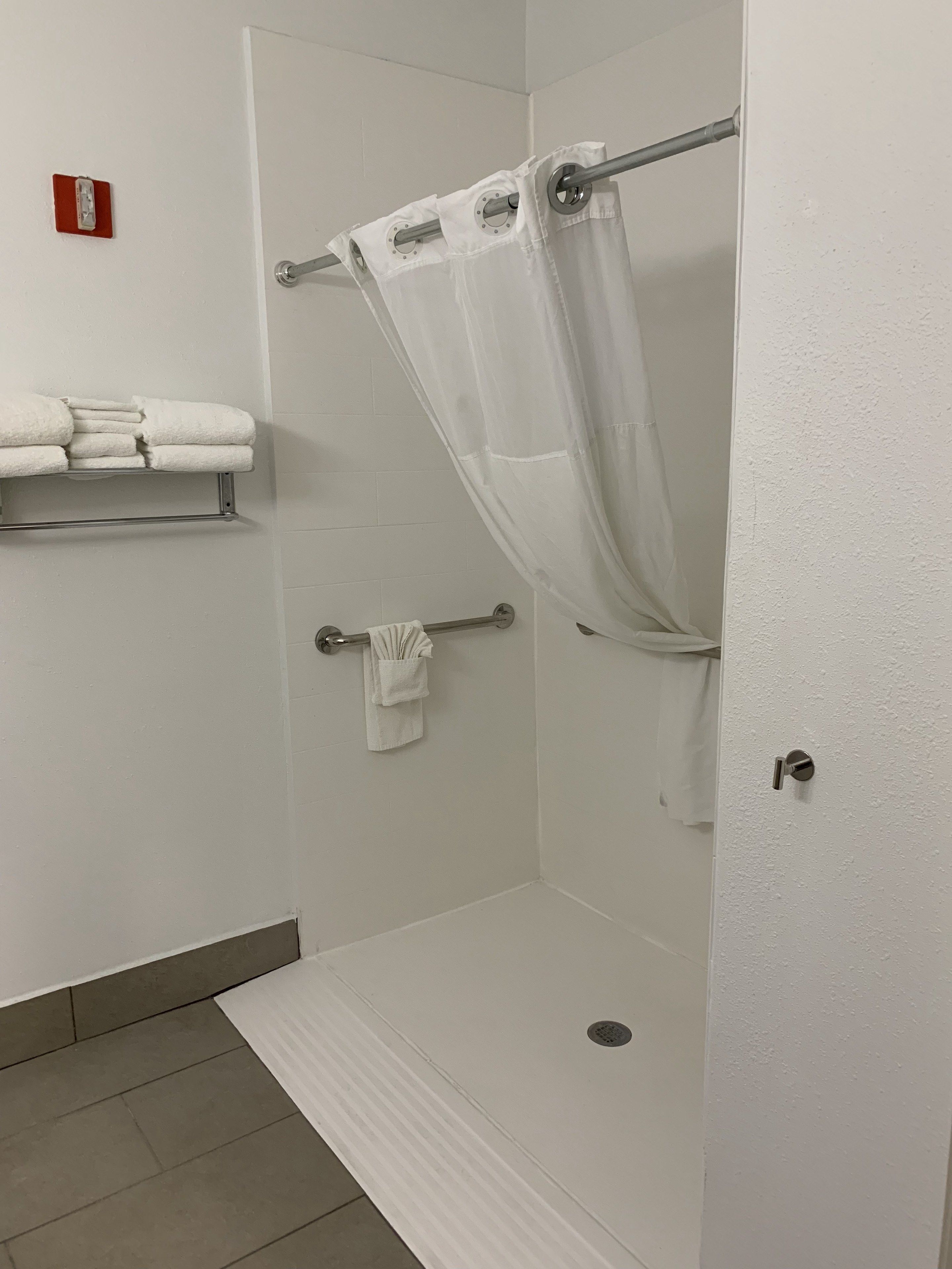 Un espacio de ducha con puerta de vidrio, un perchero con toallas dobladas y un detector de incendios en la pared.