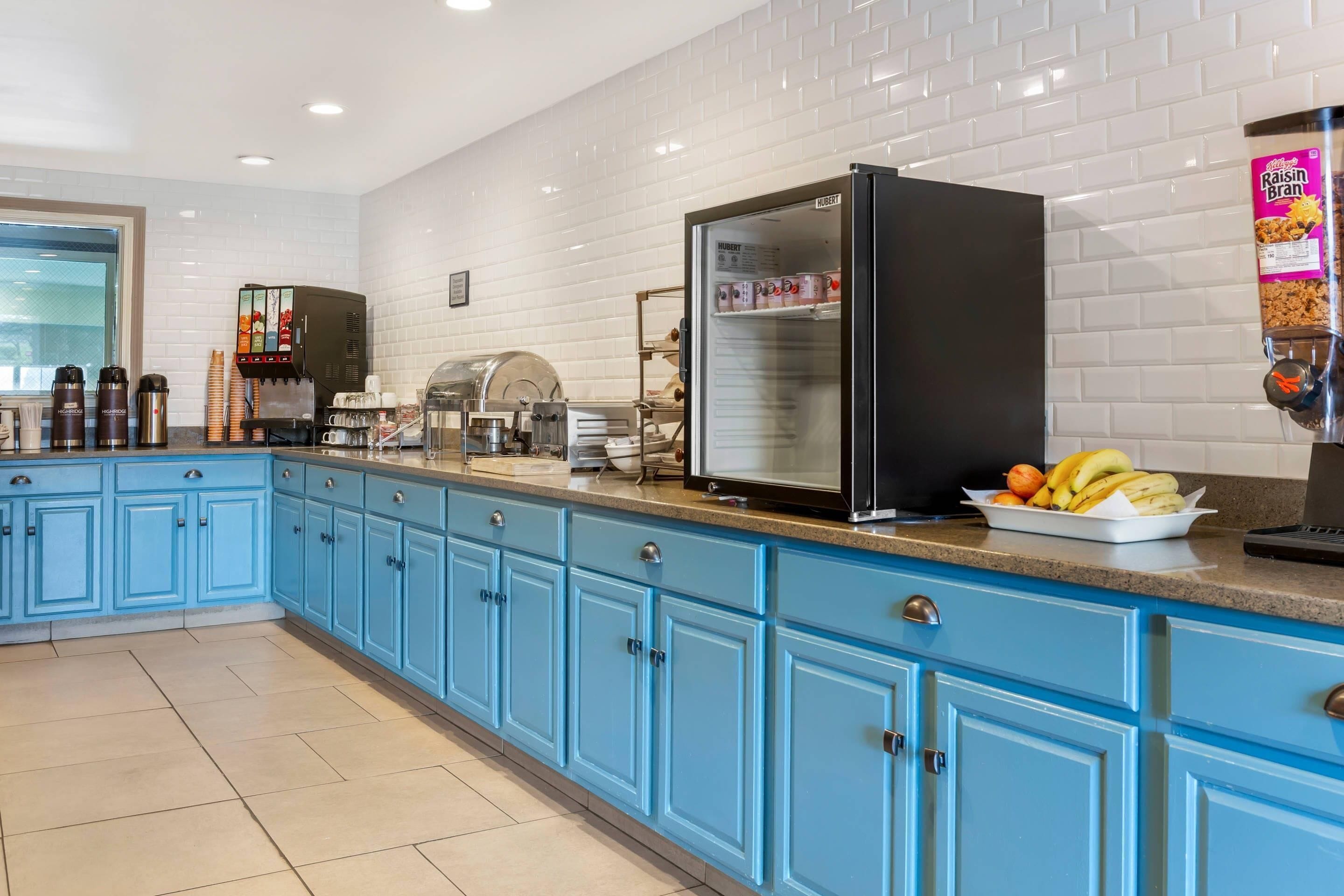 Una cocina con gabinetes azules, un refrigerador, una máquina de café y un bol de fruta sobre la encimera.