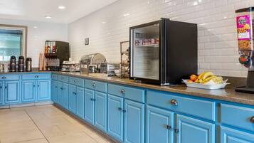Una cocina con gabinetes azules, un refrigerador, una máquina de café y un bol de fruta sobre la encimera.