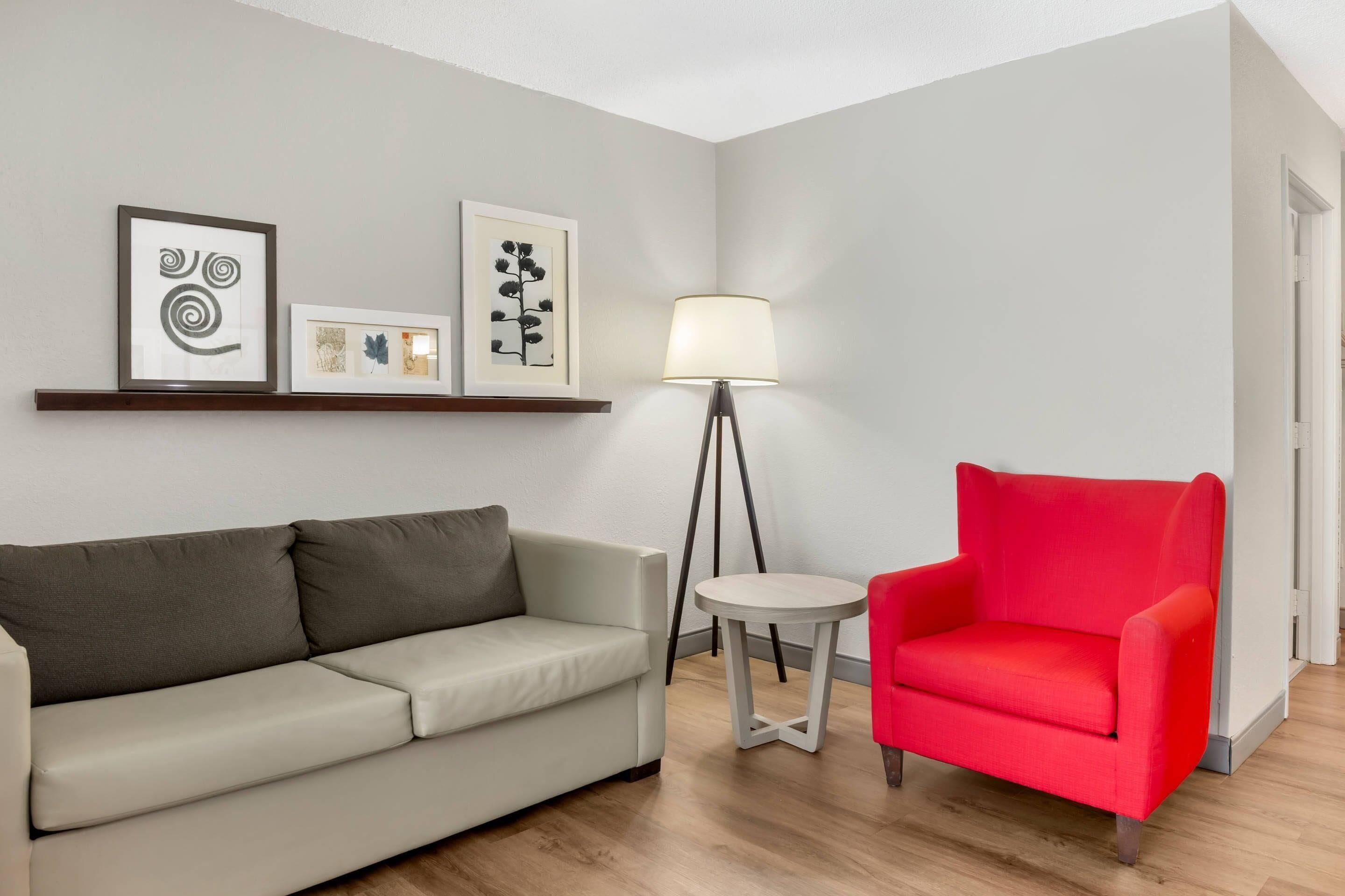 A room with a grey sofa, a red armchair, a floor lamp, and framed artwork on the wall.