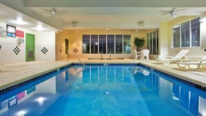 An indoor swimming pool with clear blue water, a green exit door, and white lounge chairs along the poolside. - Country Inn & Suites by Radisson, Hiram, GA (Hiram)