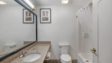 Un baño con encimera de granito, un lavamanos blanco, inodoro, un cuadro en la pared y cortina de ducha.