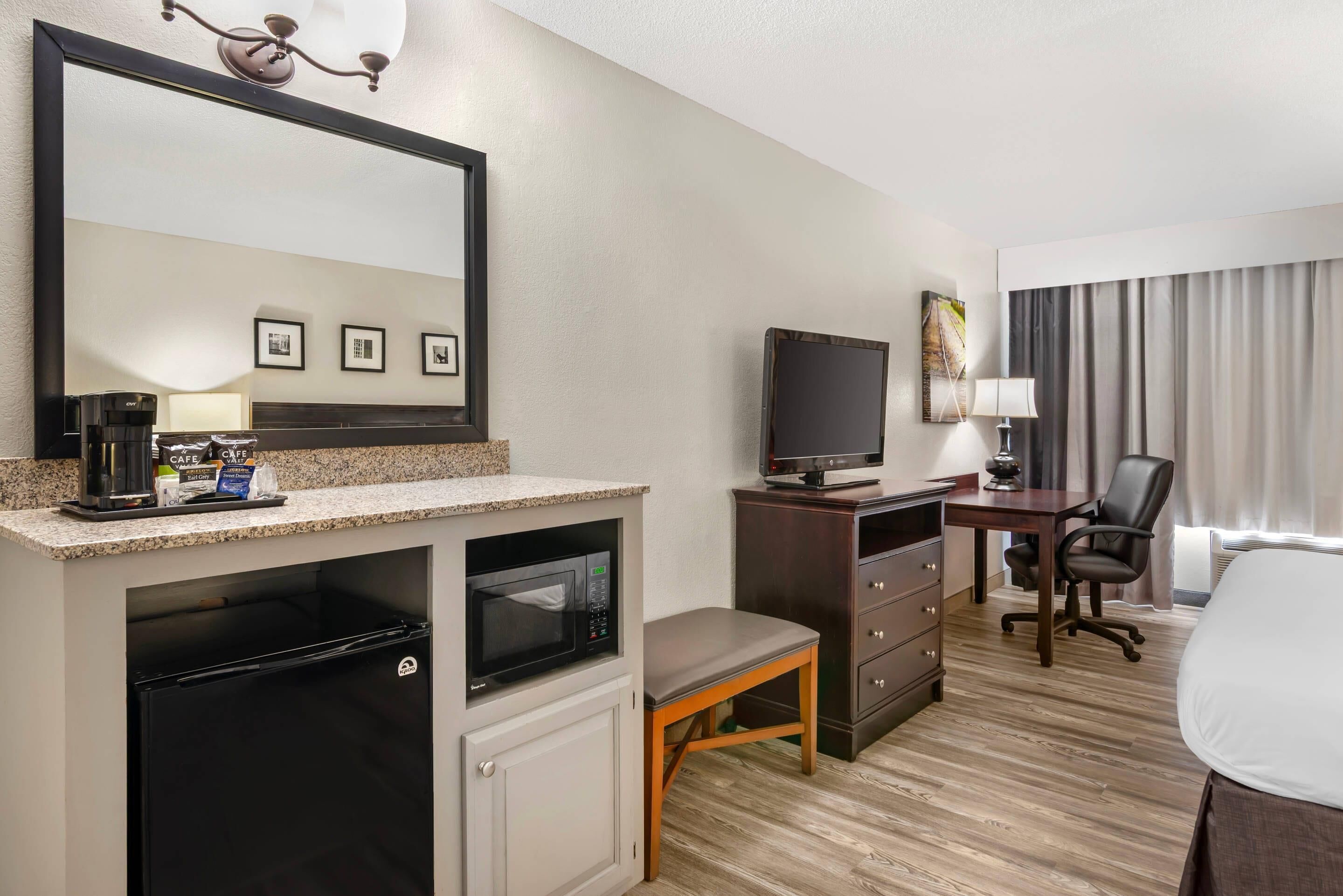 Hotelkamer met kitchenette, flatscreen-televisie, bureau met stoel, bed en grote spiegel.