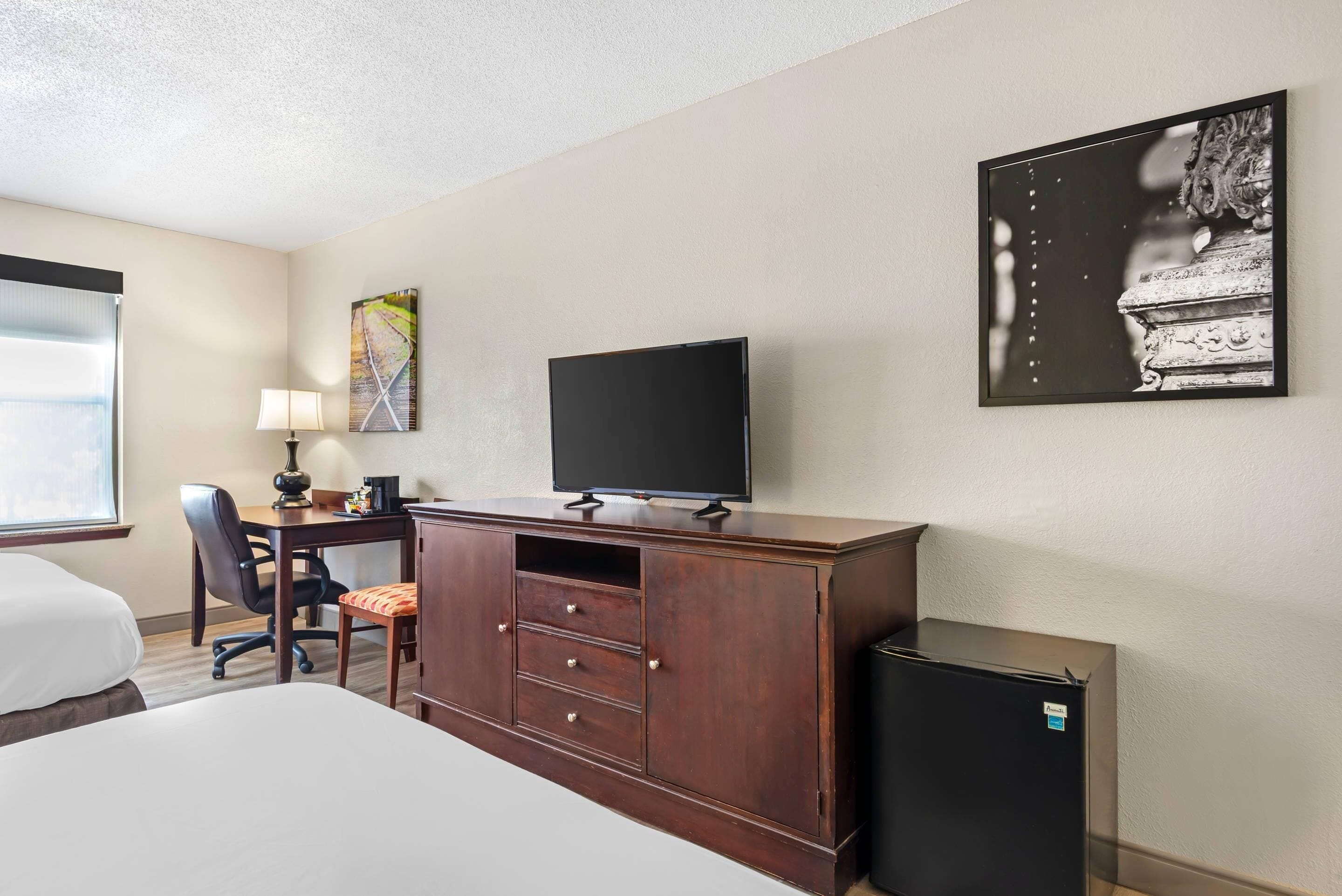 A hotel room with a bed, a desk with a chair, a television, a cabinet, and a refrigerator.