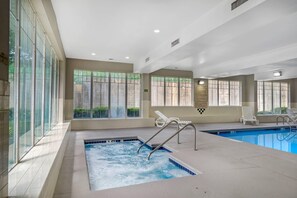 An indoor swimming pool with clear glass walls, a hot tub, and lounge chairs. - Country Inn & Suites by Radisson, Hiram - Atlanta Northwest (Hiram)