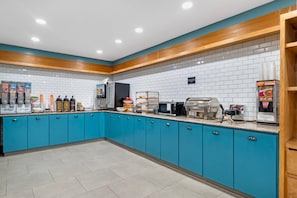 Un área de cocina con gabinetes verde azulado, salpicadero de azulejos blancos y varios electrodomésticos, incluyendo una cafetera, microondas y tostadora.