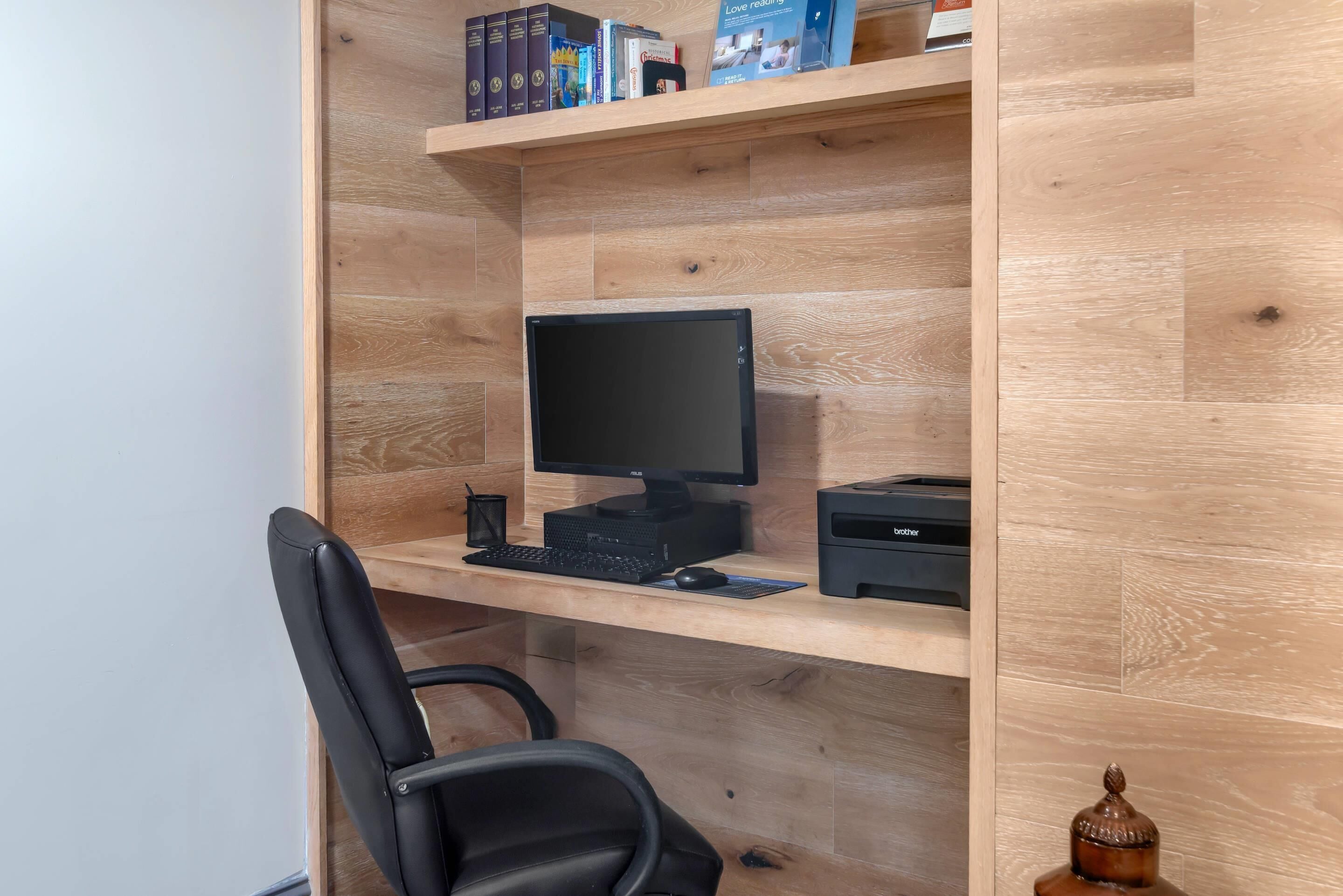 A wooden desk with a computer setup including a monitor, keyboard, and printer.
