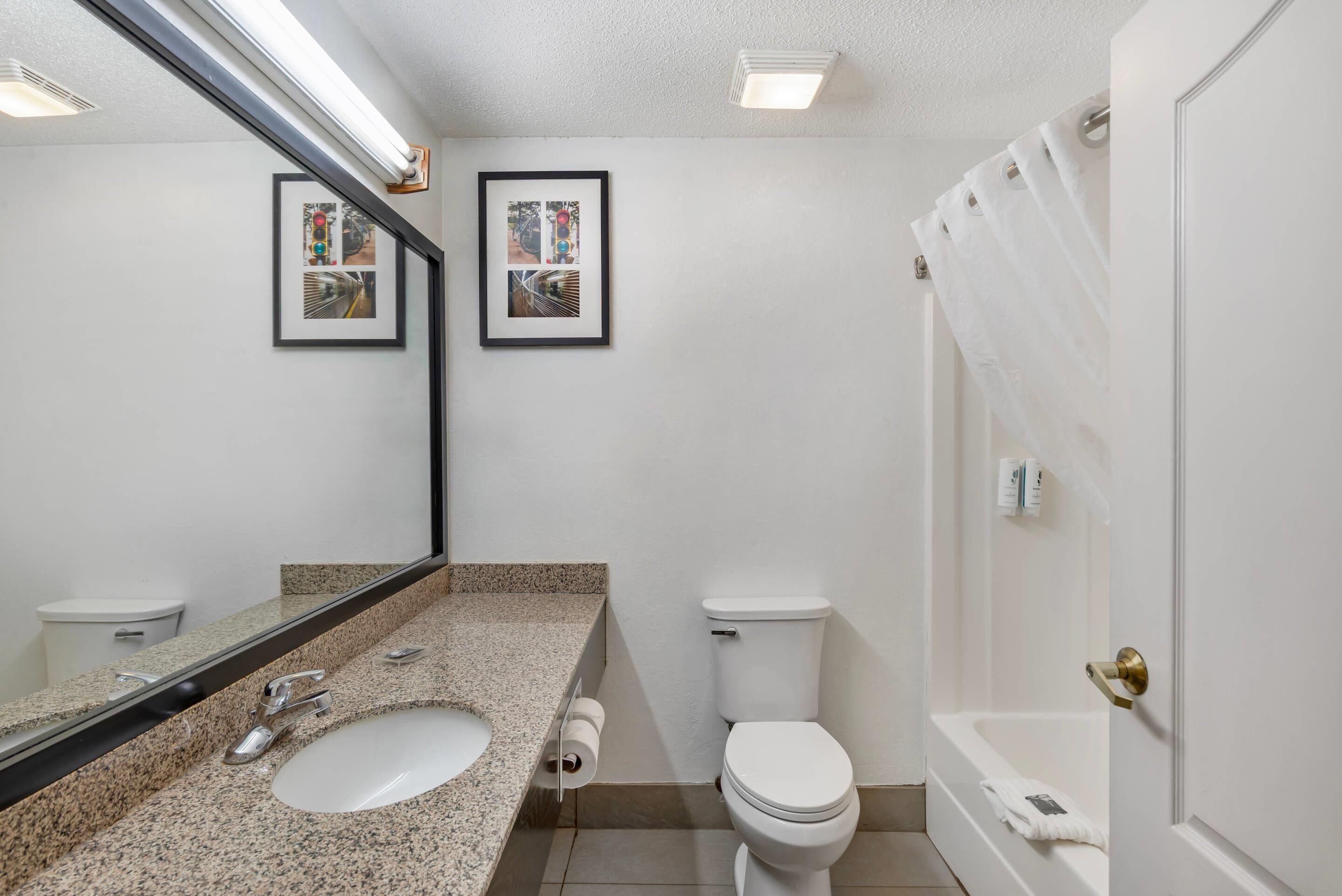 A bathroom with a granite countertop sink, a toilet, a bathtub, and two framed pictures on the wall.