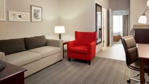 A hotel room with a sofa, a red armchair, a desk, and a lamp. - Country Inn & Suites by Radisson, Hiram, GA (Hiram)