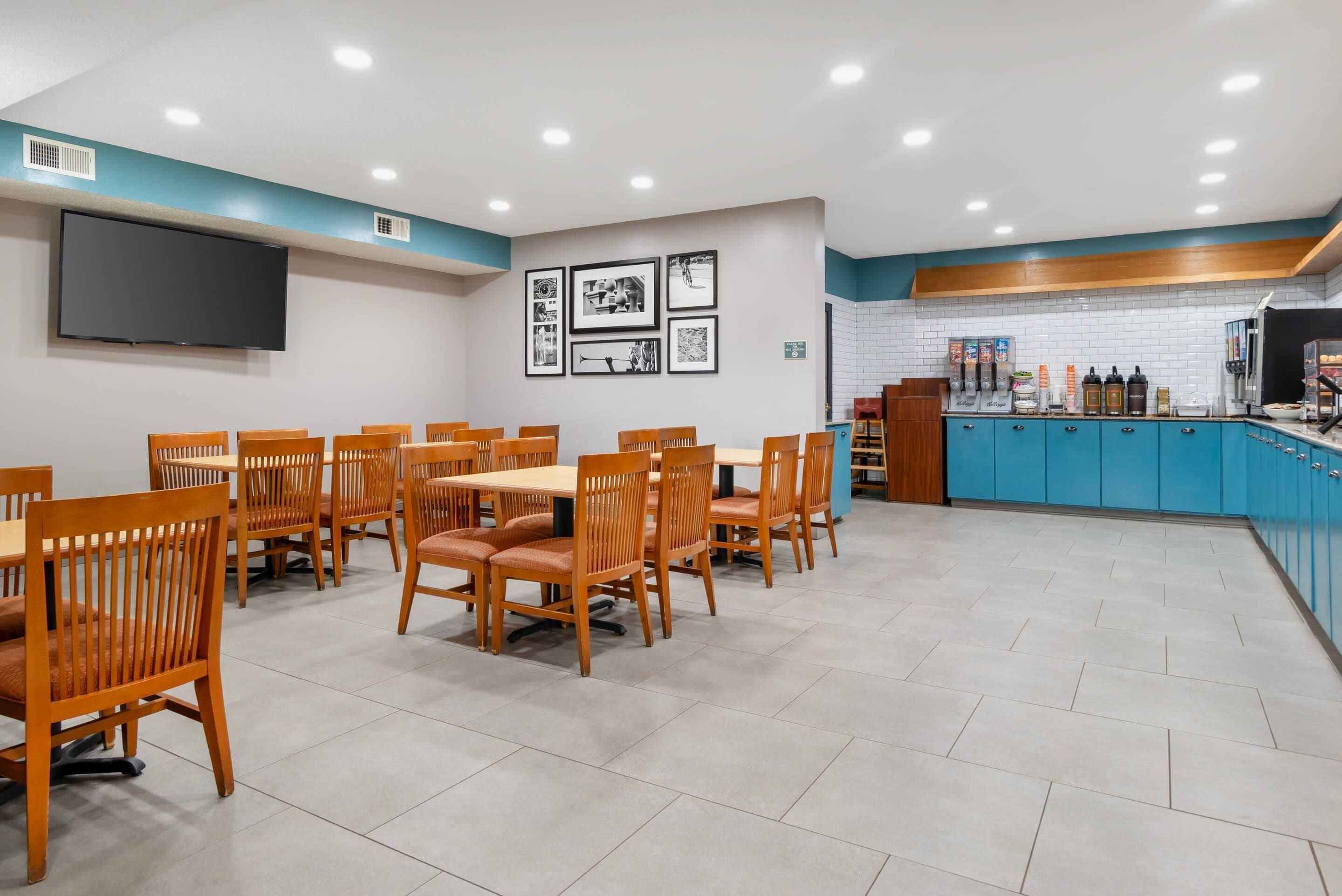 A restaurant with wooden tables and chairs, a kitchen area with blue cabinets, and a flat-screen TV mounted on the wall.