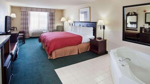 A hotel room with a large bed, a desk with a chair, a desk lamp, a nightstand with a lamp, a bathroom with a bathtub, and a large mirror. - Country Inn & Suites by Radisson, Hiram, GA (Hiram)