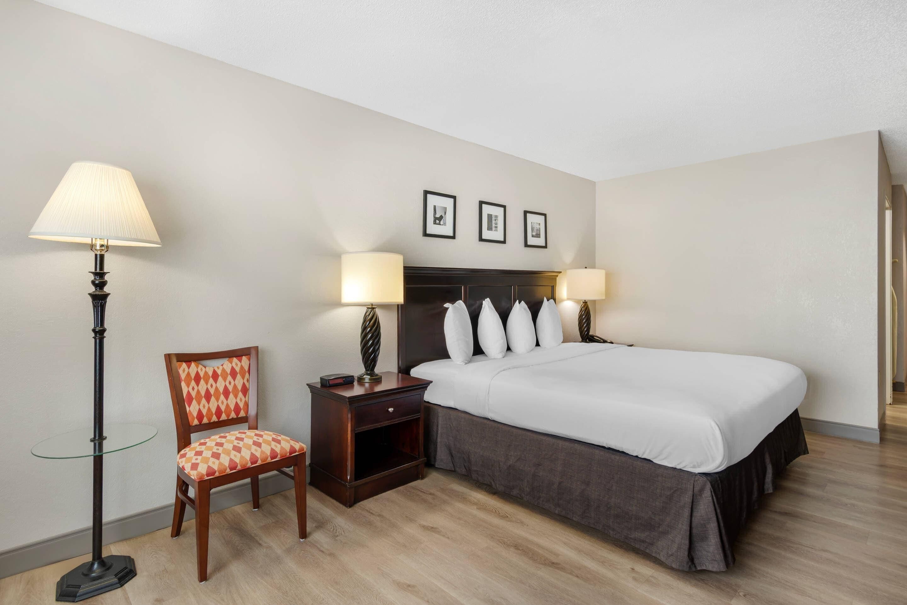 A hotel room with a bed, two bedside lamps, a chair, a nightstand, and three framed pictures on the wall.