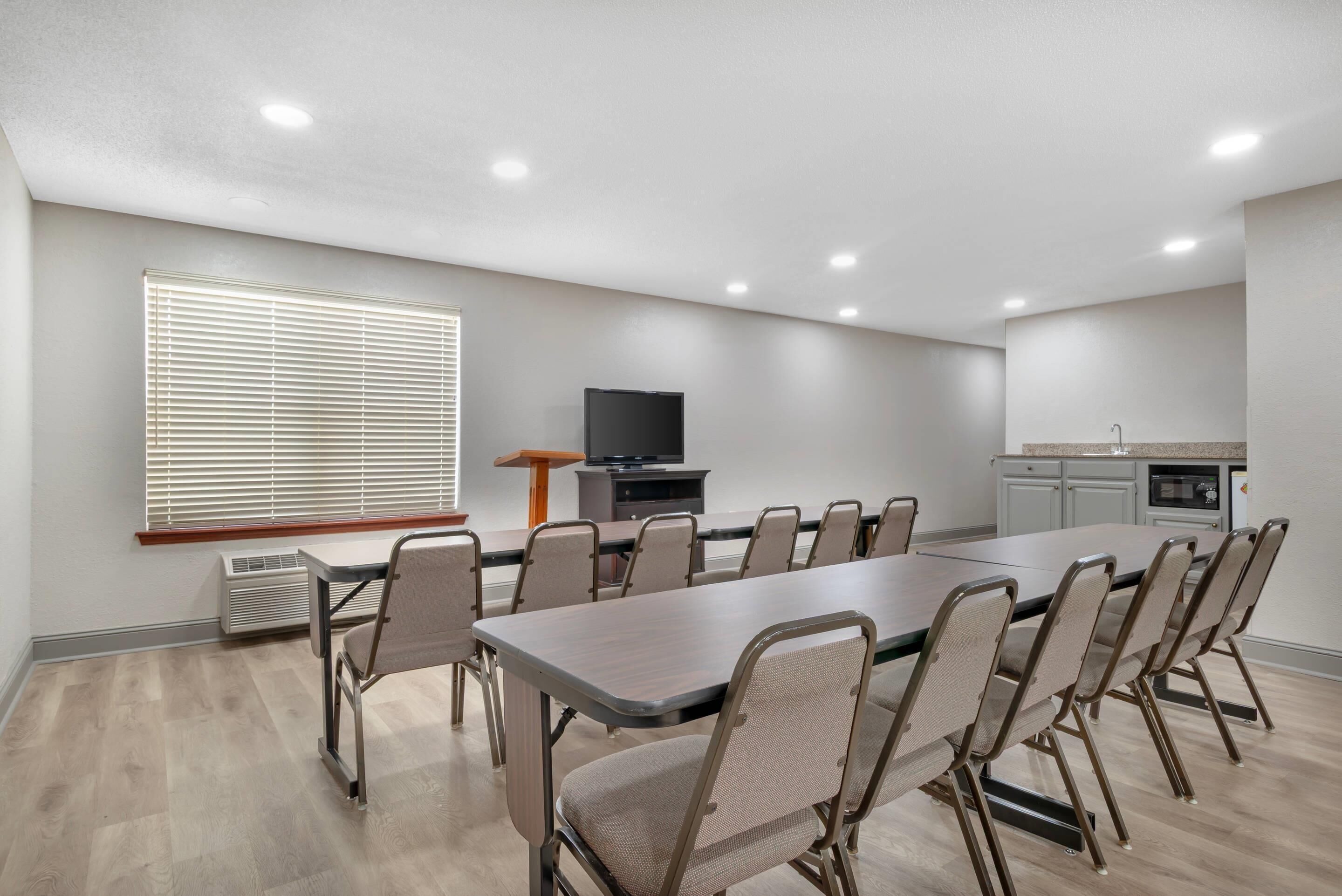 A conference room with a long table and chairs, a television, and a kitchenette.
