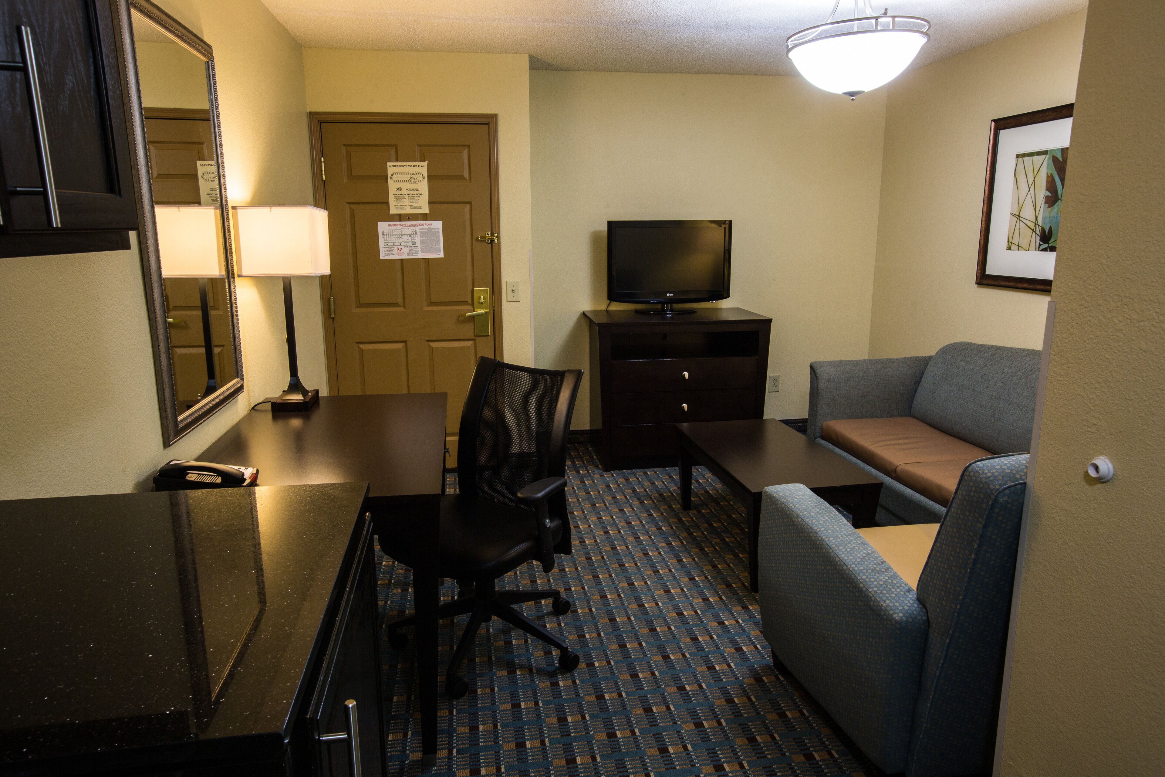A hotel room with a desk, chair, television, sofa, and a patterned carpet.