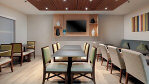 A modern dining area with a long table, chairs, a flat-screen TV, and a sofa. - Holiday Inn Express Alpharetta - Roswell by IHG (Alpharetta)